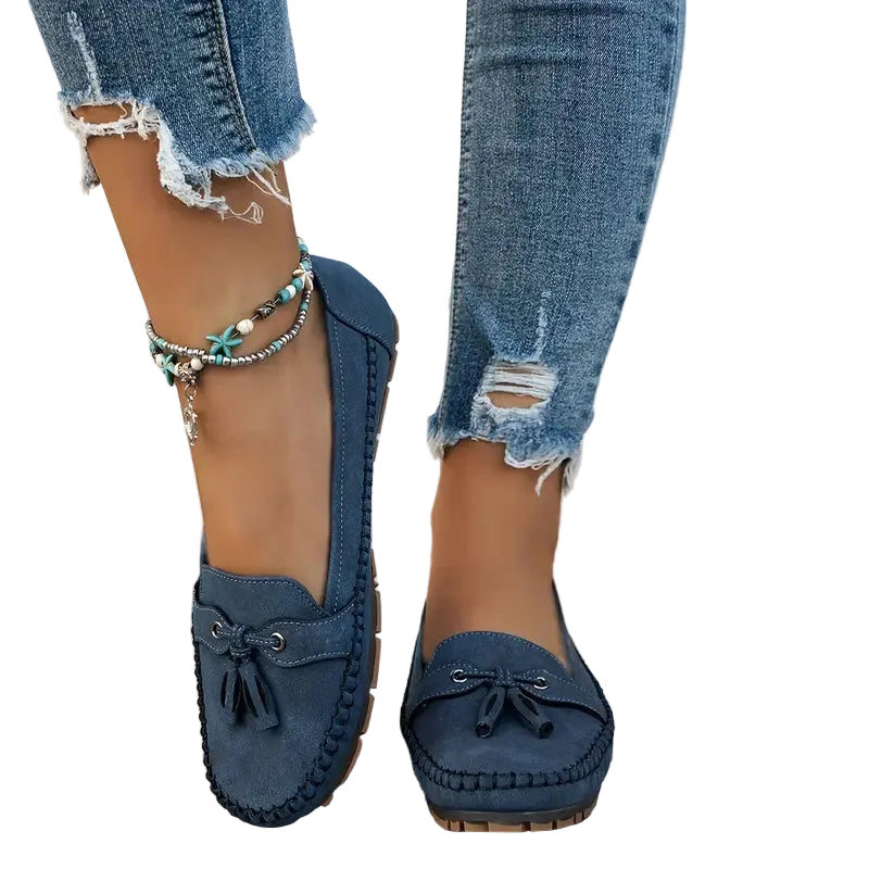 Des mocassins plats en suède bleu marine, dotés d'un nœud décoratif à l'avant et d'une semelle en caoutchouc pour un confort optimal. Ce modèle est parfait pour un look décontracté, chic et moderne, accompagné d'un jean déchiré et de bracelets bohèmes. Un choix idéal pour allier style et confort.