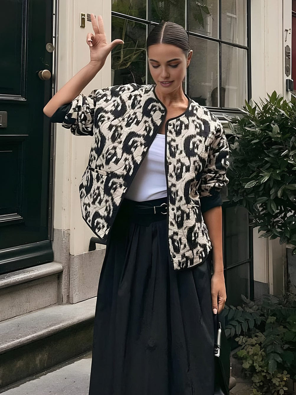 Manteau ajusté à sequins Prylia pour invitées de mariage, porté par une modèle avec un look élégant et moderne. Le manteau présente un motif animalier noir et blanc, parfait pour une occasion spéciale. Il est associé à une jupe fluide noire et un top blanc, créant une tenue chic et raffinée.