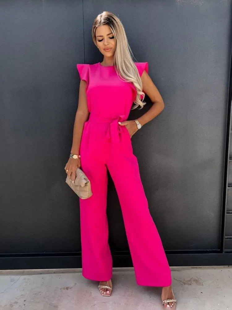Combinaison rose vif pour femme avec des manches volantées et une coupe large. Elle est dotée d'une taille élastiquée et est accompagnée d'une pochette beige et de sandales à talons, offrant un look moderne et élégant pour une occasion spéciale.