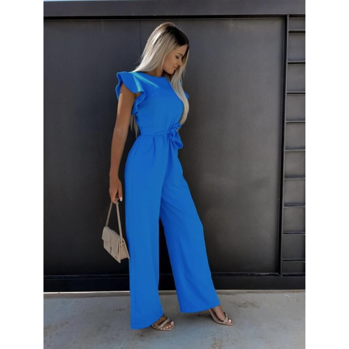 Combinaison bleu vif pour femme avec des manches volantées et une ceinture à la taille, offrant une coupe large et élégante. Elle est accompagnée d'un petit sac beige et de sandales à talons, parfaites pour un look moderne et raffiné.