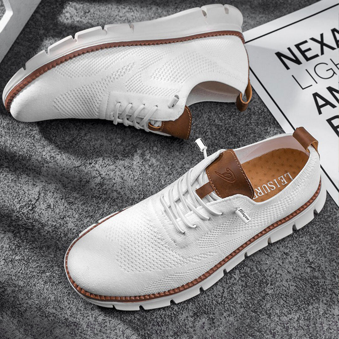 Paire de chaussures urbaines blanches en maille respirante avec lacets, détails en simili cuir camel et semelle épaisse crantée, posée sur un sol gris.
