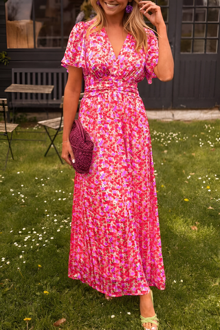 Robe longue à col en V pour femme, modèle tendance. Cette robe légère et fluide est décorée d'un motif floral vibrant dans des tons de rose et fuchsia, parfaite pour les journées d'été. Elle est complétée par un sac en crochet violet et des boucles d'oreilles assorties, offrant un look à la fois élégant et décontracté.