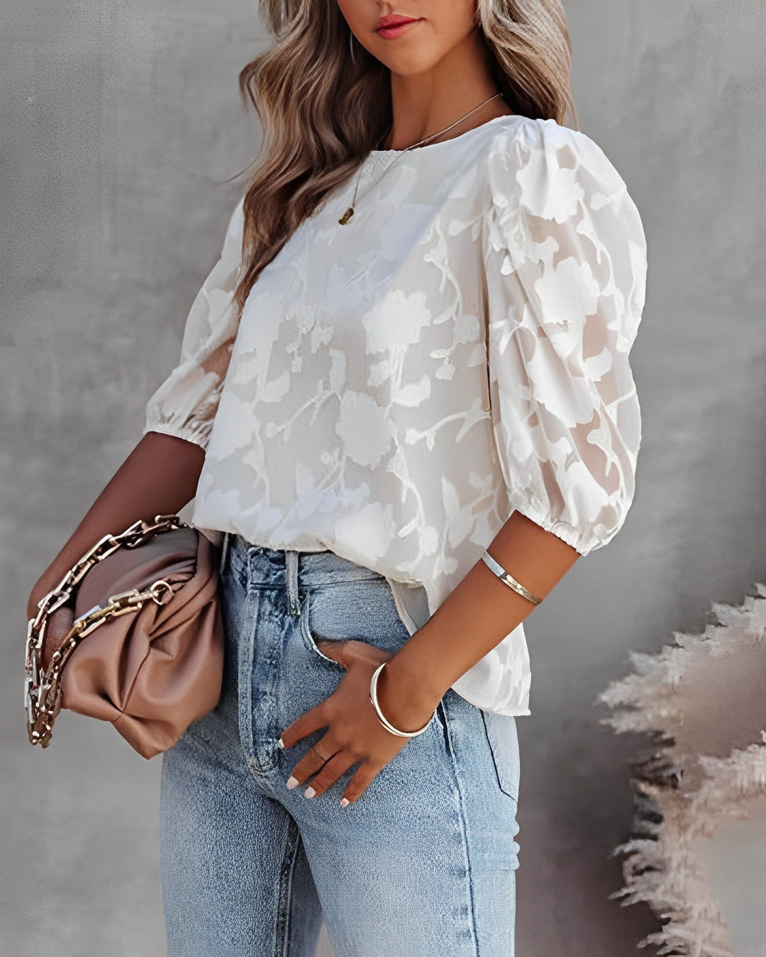 Chemisier pour femme, léger et élégant, avec un imprimé floral ton sur ton sur fond blanc. Ce haut à manches bouffantes est porté avec un jean décontracté, créant une tenue à la fois chic et moderne. Parfait pour un look tendance et confortable, idéal pour les sorties quotidiennes ou les journées ensoleillées.