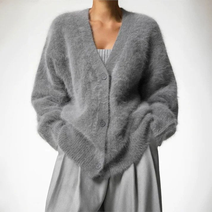 Femme portant un cardigan duveteux gris au style ample, boutonné sur le devant, assorti à un pantalon fluide de la même teinte, dans un décor épuré et lumineux.