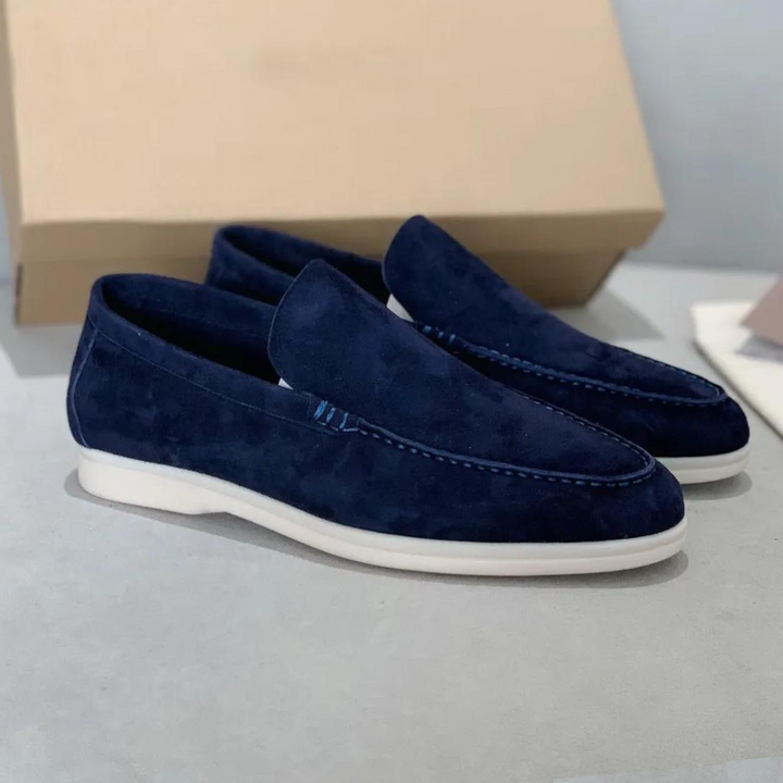 Mocassins en daim bleu marine avec une finition élégante, des détails subtils et une semelle blanche, créant un look moderne et raffiné.