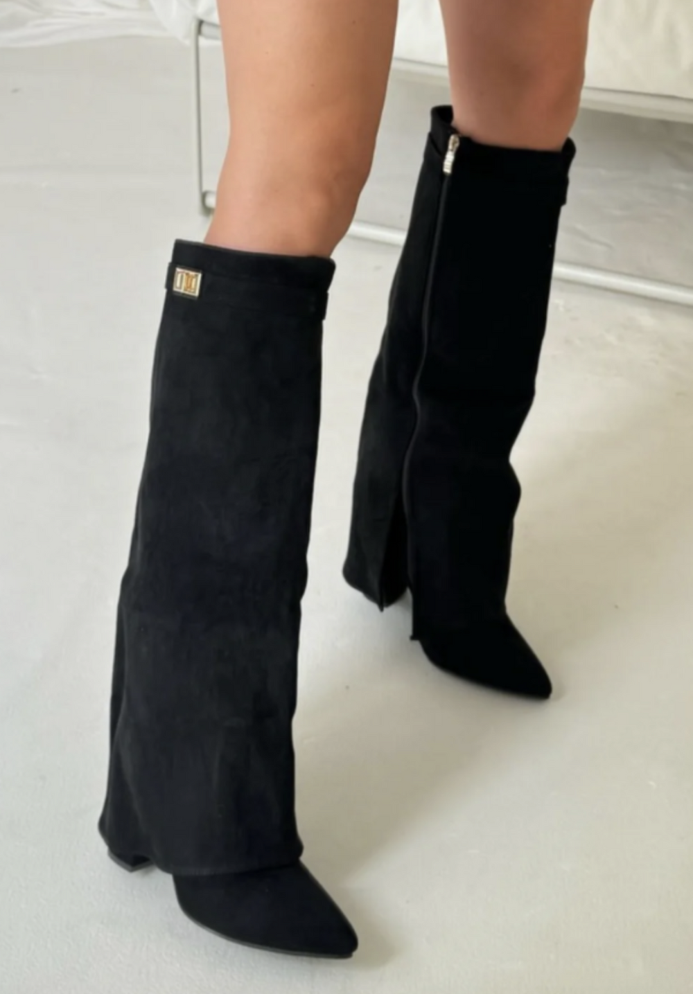 Bottes noires mi-mollet à bout pointu avec fermeture éclair sur le côté et petit détail métallique, portées avec talon.