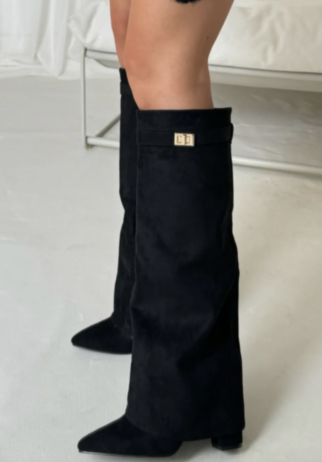 Bottes noires à bout pointu, coupe mi-mollet avec revers et détail doré, talon moyen, portées sur fond clair.