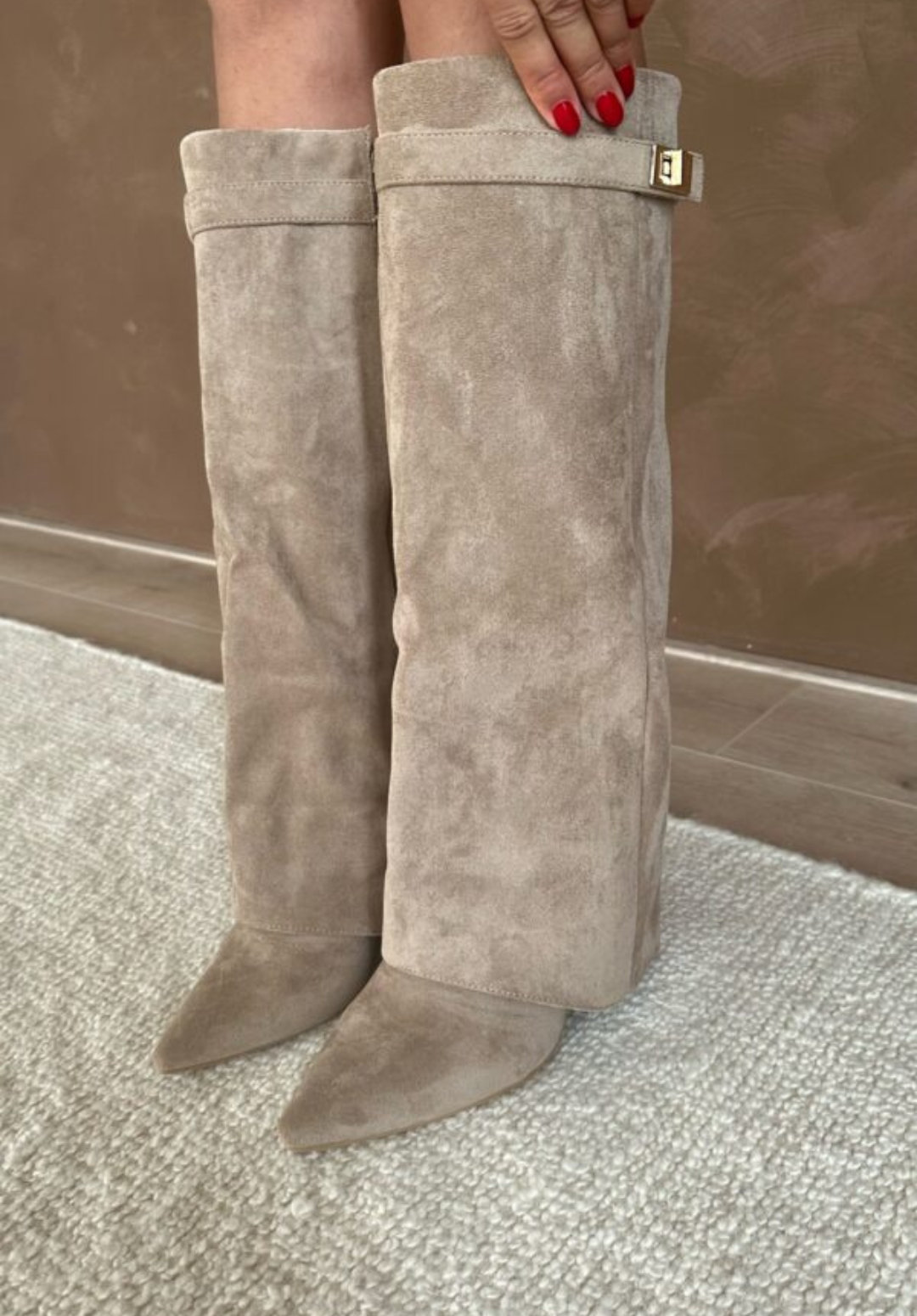 Bottes beige taupe effet daim à bout pointu, coupe mi-mollet avec revers et boucle dorée, portées debout sur tapis.