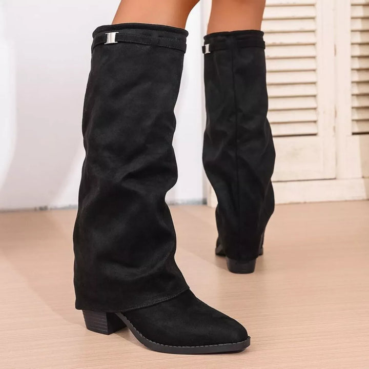 Bottes noires pour femme au style tendance, présentant une tige longue et souple, un petit talon carré et un détail métallique discret sur le haut, offrant un look moderne et élégant.