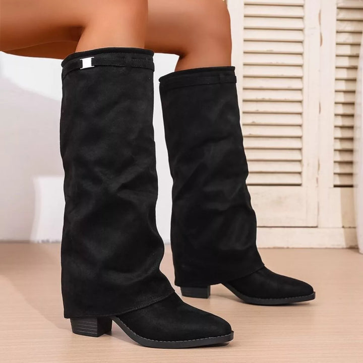 Bottes noires pour femme au style moderne, avec tige haute souple, petit talon carré et détail métallique discret près du haut, créant un look chic et tendance pour toutes les tenues.
