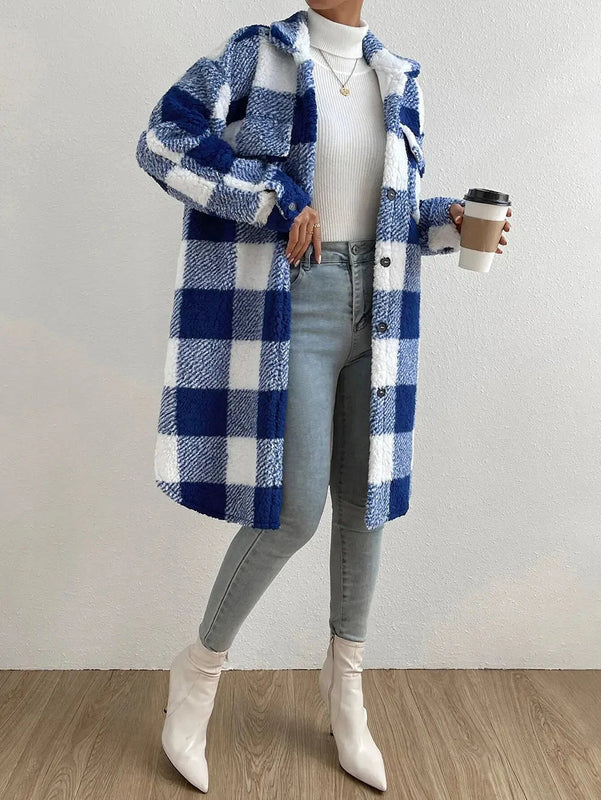Une femme porte un manteau long à carreaux bleu et blanc en peluche, avec des manches longues et un col classique. Le manteau est boutonné sur le devant et est accompagné d'un turtleneck blanc, de jeans clairs et de bottines blanches à talons. Elle tient un café à la main, créant un look moderne, élégant et décontracté, parfait pour une sortie en ville par temps frais.