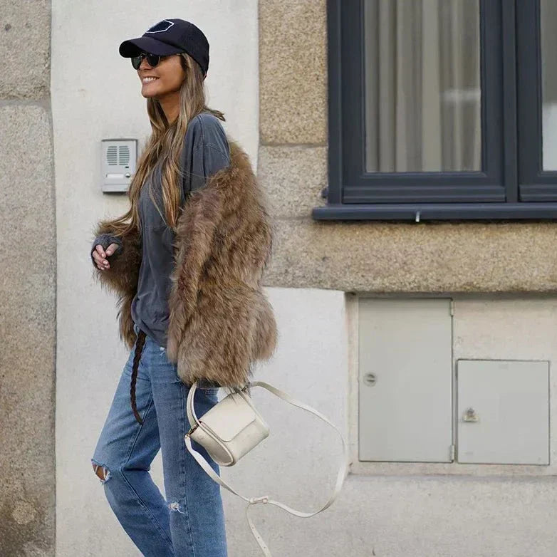 Style urbain décontracté avec veste en fausse fourrure, jean usé et casquette.