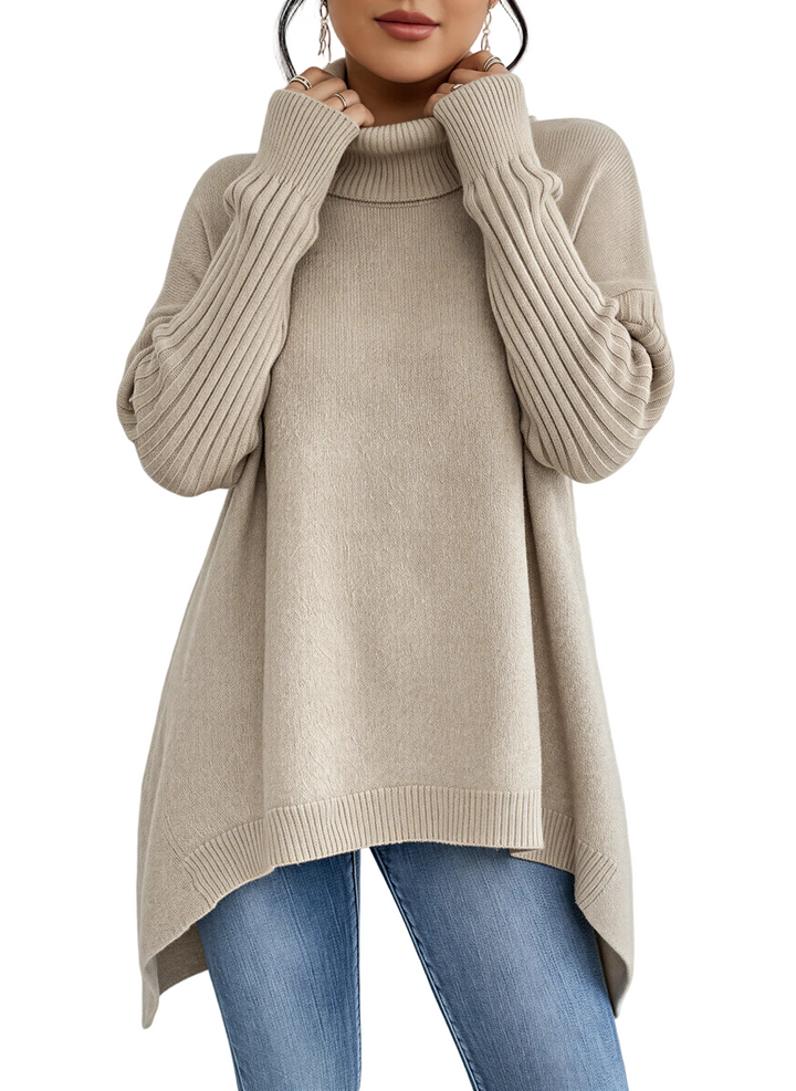 Une femme porte un pull à col roulé beige ample à manches longues côtelées. Ce haut fluide et légèrement asymétrique est associé à un jean bleu pour un look élégant, moderne et confortable, idéal pour l'automne/hiver.