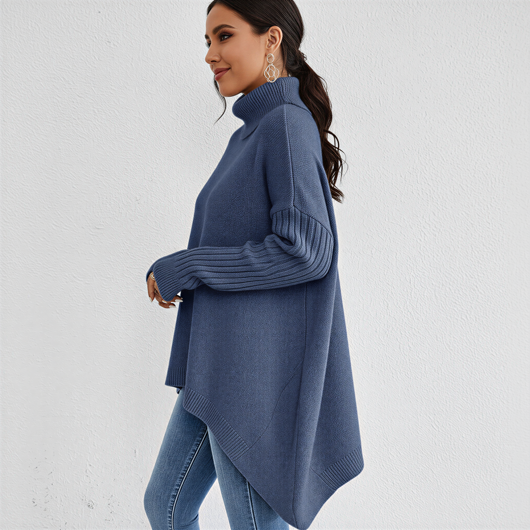 Femme de profil portant un pull à col roulé bleu, à la coupe ample et fluide, avec des manches longues côtelées. Le vêtement présente un ourlet asymétrique allongé à l’arrière et est associé à un jean ajusté bleu clair. Un style élégant et décontracté parfait pour la saison automne-hiver.