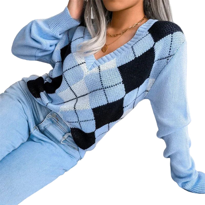 Une femme porte un pull à col en V en maille douce, orné d’un motif à losanges de style argyle dans les tons bleu clair, noir et blanc. Le pull présente une coupe décontractée avec des manches longues et des bords côtelés, associé à un jean bleu clair. L’ensemble dégage un style moderne et confortable, idéal pour les journées d’hiver.