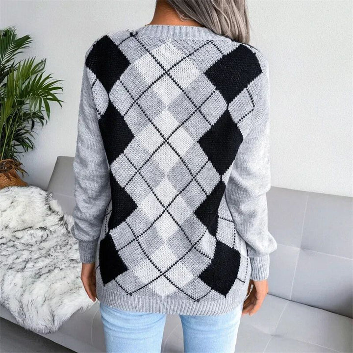 Vue de dos d’une femme portant un pull en maille gris à motif losange de style argyle, dans des tons de gris clair, gris foncé et noir. Le pull présente des manches longues et une coupe droite, mettant en valeur le motif géométrique sur toute la surface du dos. L’ensemble crée un look moderne et confortable, parfait pour la saison hivernale.