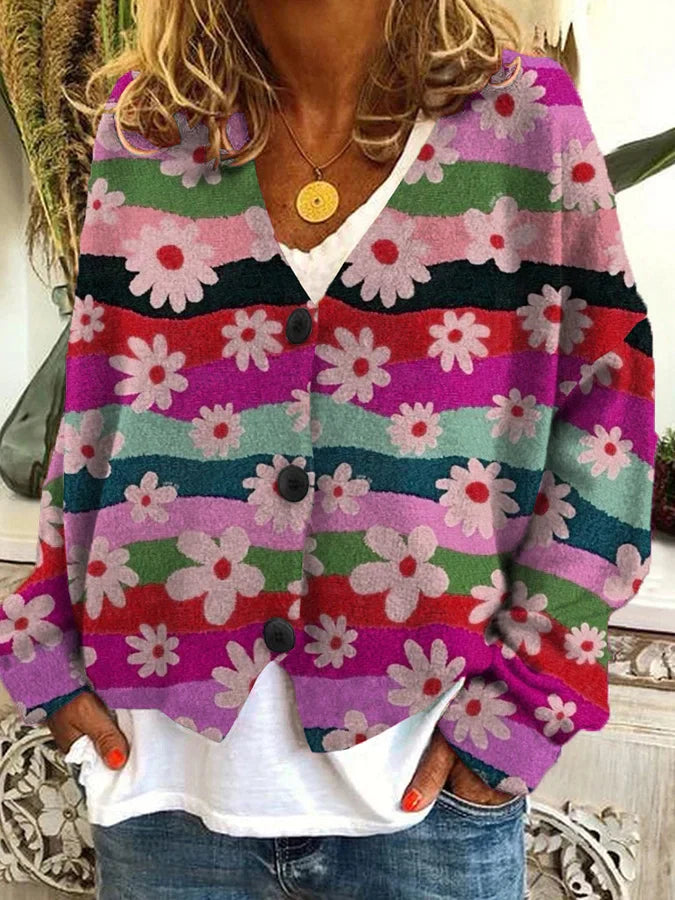 Femme portant un cardigan à motifs floraux multicolores avec de larges rayures ondulées en rose, vert, rouge, bleu et violet. Le vêtement est boutonné sur le devant avec trois gros boutons noirs et se porte sur un t-shirt blanc et un jean décontracté. Le style est bohème et vintage, idéal pour un look coloré et original au quotidien.