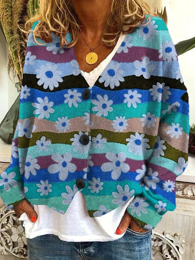 Femme portant un cardigan à motifs floraux colorés avec des rayures ondulées bleues, vertes et violettes. Le gilet présente de grands boutons noirs et un col en V, porté sur un t-shirt blanc décontracté et un jean bleu. Le vêtement dégage un style vintage et confortable, parfait pour un look casual et élégant.
