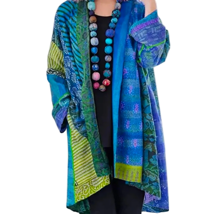 Femme portant un cardigan long et ample au style tendance, avec motifs norvégiens multicolores dans des tons de bleu, vert et turquoise, manches longues et coupe fluide, porté ouvert sur une tenue sombre pour une allure artistique et bohème.