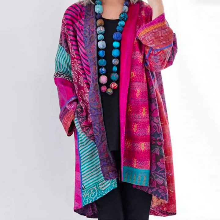 Femme portant un cardigan long et ample au style tendance, avec motifs norvégiens multicolores dans des tons de rose, violet, turquoise et bleu, manches longues et coupe fluide, porté ouvert sur une tenue sombre pour une allure bohème et artistique.