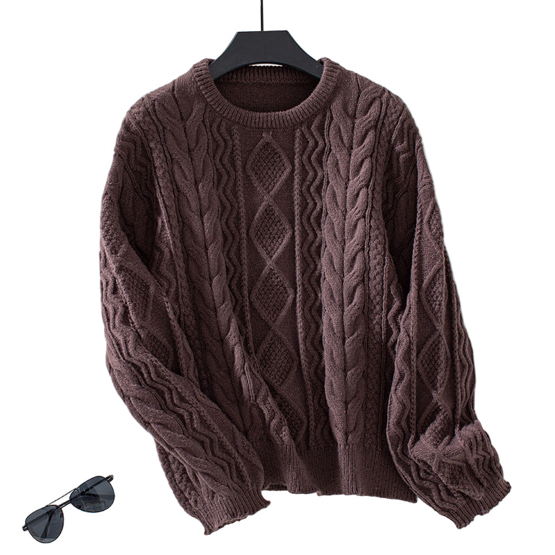 Pull en maille torsadée de couleur marron chocolat, au motif géométrique en losanges sur le devant. Le tissu épais et texturé met en avant des torsades élégantes et un tricot dense, parfait pour un style chaud et confortable. Présenté sur un cintre noir contre un fond blanc lumineux, le pull se distingue par ses manches longues légèrement bouffantes et ses finitions côtelées au col, aux poignets et à la taille. Une paire de lunettes de soleil posée à côté apporte une touche moderne à la mise en scène.