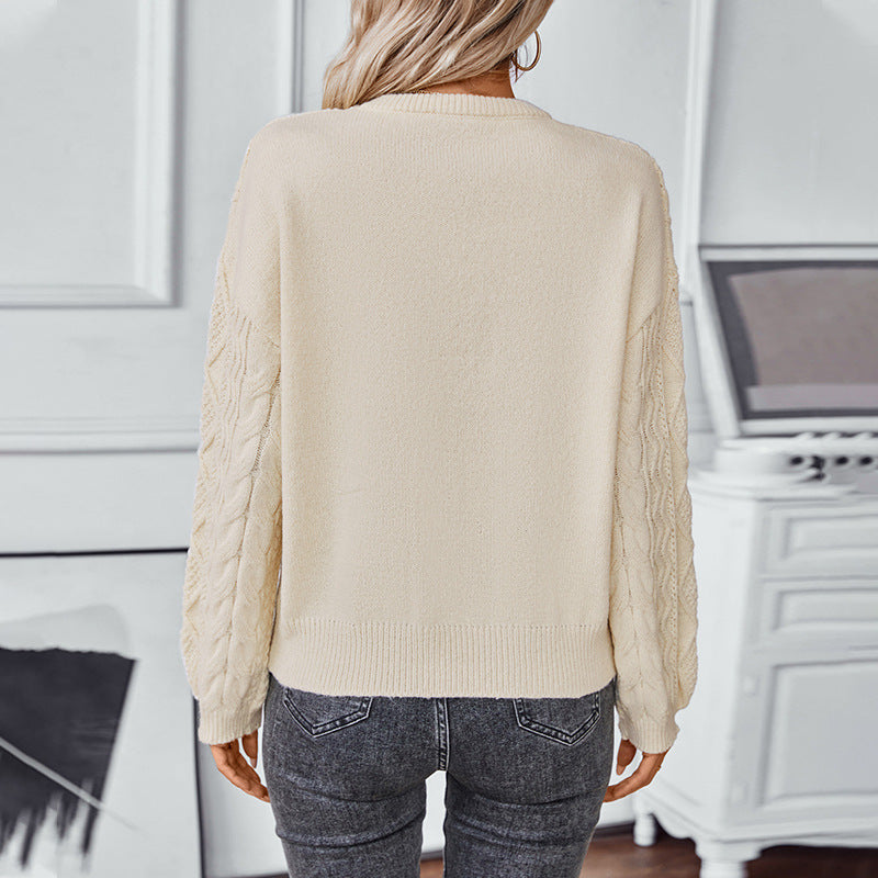 Vue de dos d'une femme portant un pull blanc à manches longues en maille torsadée. Le dos du vêtement est lisse, contrastant avec la texture des manches. La maille, à la coupe droite et aux bords-côtes, offre un style à la fois simple et élégant. Le pull est associé à un jean foncé, créant une allure moderne et décontractée dans un intérieur lumineux et raffiné.