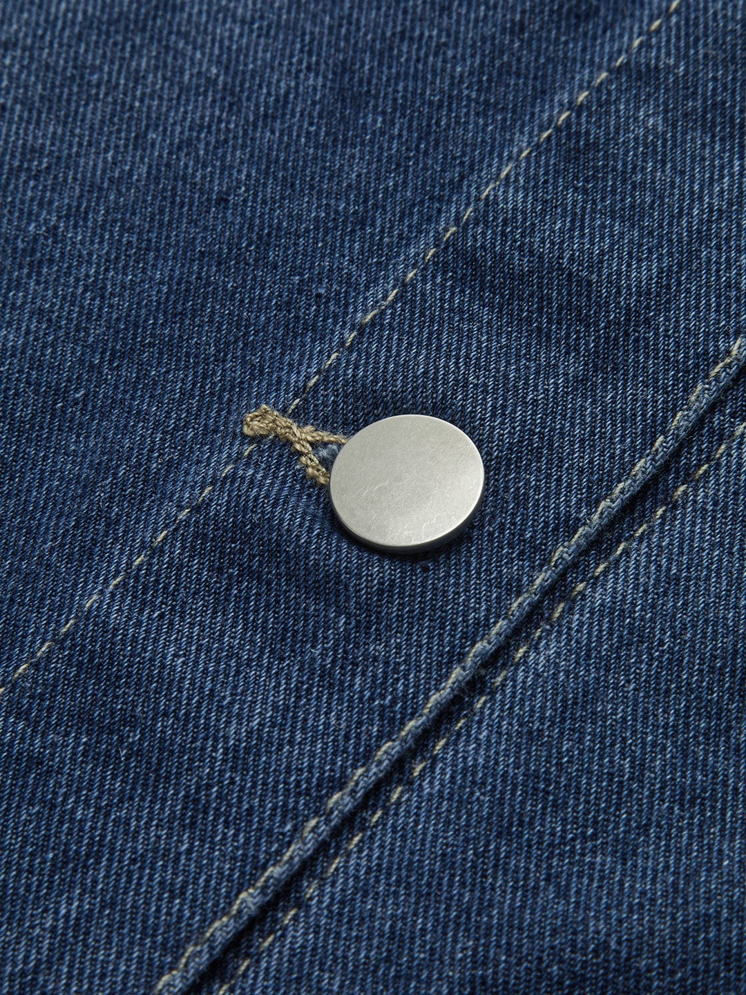 Détail du bouton métallique de la veste en jean 'Sylpha' pour femme, mettant en valeur la qualité du tissu en denim bleu et la finition soignée. Ce zoom sur le bouton illustre l'attention portée aux détails dans le design moderne de cette veste décontractée.