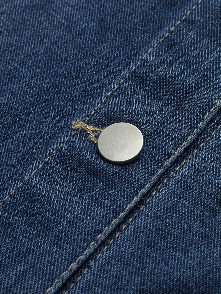 Détail du bouton métallique de la veste en jean 'Sylpha' pour femme, mettant en valeur la qualité du tissu en denim bleu et la finition soignée. Ce zoom sur le bouton illustre l'attention portée aux détails dans le design moderne de cette veste décontractée.