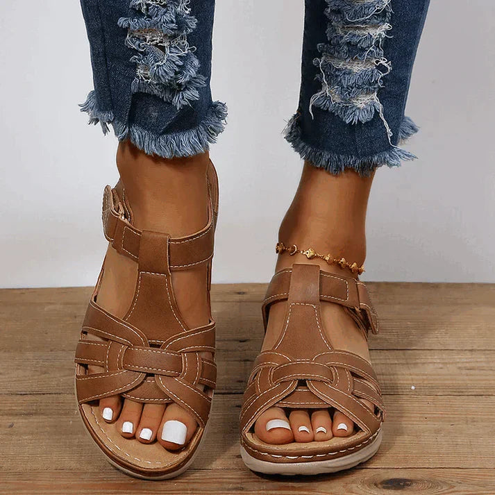 Modernes, coloris camel, brides croisées ajourées et semelle confort épaisse, vue de face portées avec un jean sur sol en bois.