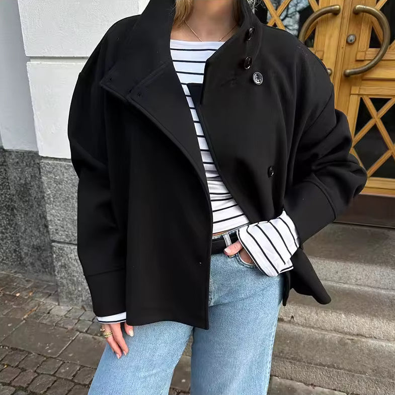 Femme vêtue d’un manteau court noir à double boutonnage, associé à un t-shirt rayé blanc et noir et à un jean bleu clair. Le manteau présente une coupe moderne avec un col large et des boutons élégants, créant un look à la fois décontracté et raffiné. L’ensemble offre une allure chic et citadine parfaite pour la mi-saison.