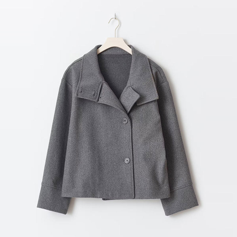 Manteau court pour femme de couleur grise, à double boutonnage avec un col large et des manches longues. Sa coupe droite et minimaliste lui confère un style moderne et élégant, parfait pour un look chic et urbain pendant les journées fraîches. Présenté sur un cintre, ce manteau met en avant la qualité du tissu et la simplicité de sa conception.