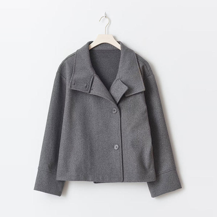 Manteau court pour femme de couleur grise, à double boutonnage avec un col large et des manches longues. Sa coupe droite et minimaliste lui confère un style moderne et élégant, parfait pour un look chic et urbain pendant les journées fraîches. Présenté sur un cintre, ce manteau met en avant la qualité du tissu et la simplicité de sa conception.