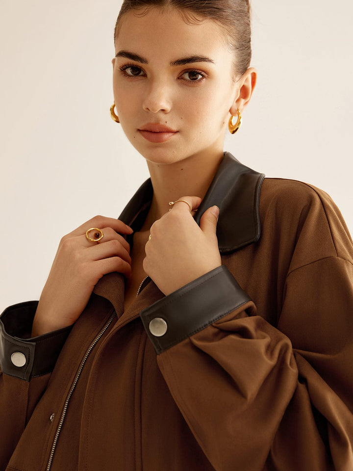 Zoom sur le col et les détails de la veste oversize 'Tiphaine' pour femme. La veste est en tissu beige avec un col en cuir noir, mise en valeur par un élégant bijou et un look moderne.