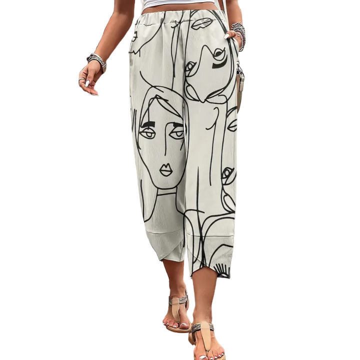 Pantalon ample pour femme à longueur mi-mollet, en tissu léger écru avec imprimé artistique de visages en lignes noires, doté d’une taille confortable et porté avec des sandales pour un style estival moderne et décontracté.