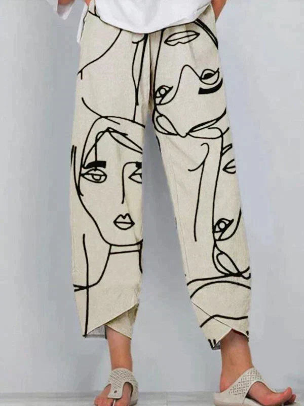 Pantalon ample pour femme à coupe droite et longueur cheville, en tissu léger écru avec imprimé artistique de visages en lignes noires, porté avec des sandales pour un look estival moderne et confortable.
