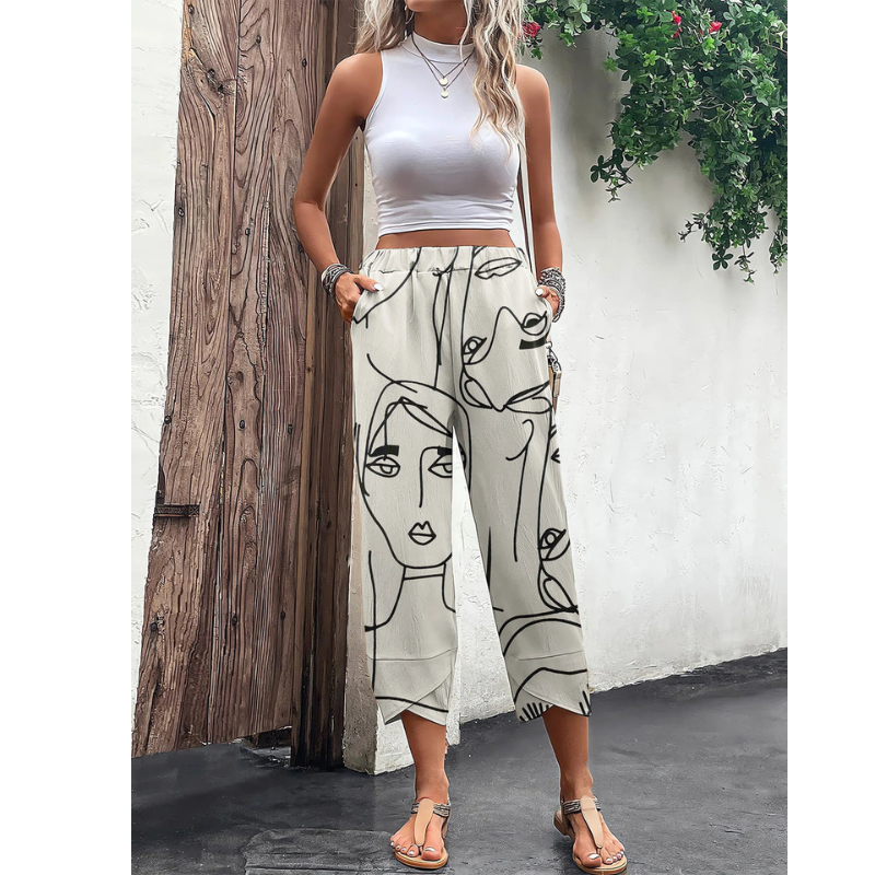 Pantalon ample pour femme porté de face, en tissu léger écru avec imprimé artistique de visages en lignes noires, doté d’une taille élastique avec cordon et de poches, associé à un haut blanc sans manches pour un style estival moderne.