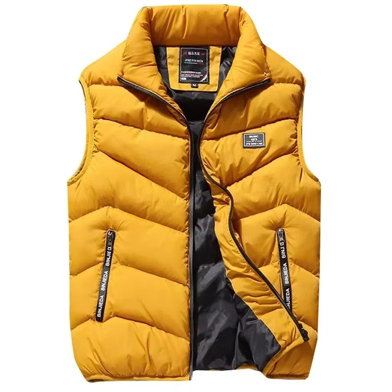Gilet matelassé pour homme de couleur jaune moutarde avec fermeture éclair noire et poches latérales zippées. Le design sans manches est doté d’un col montant et d’une doublure intérieure sombre contrastante. Ce vêtement chaud et stylé allie confort et modernité, idéal pour compléter une tenue hivernale ou décontractée.