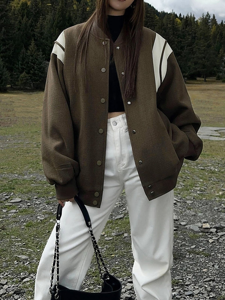 kaki olive avec empiècements crème sur les épaules, fermeture par boutons-pression argentés et poches latérales, portée avec un haut noir et un pantalon clair, look tendance en extérieur urbain.
