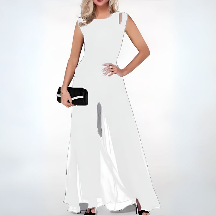 Combinaison d’été Ursuline pour femme, blanche style fête, coupe longue fluide avec voile léger et épaules ajourées, portée avec pochette et talons.