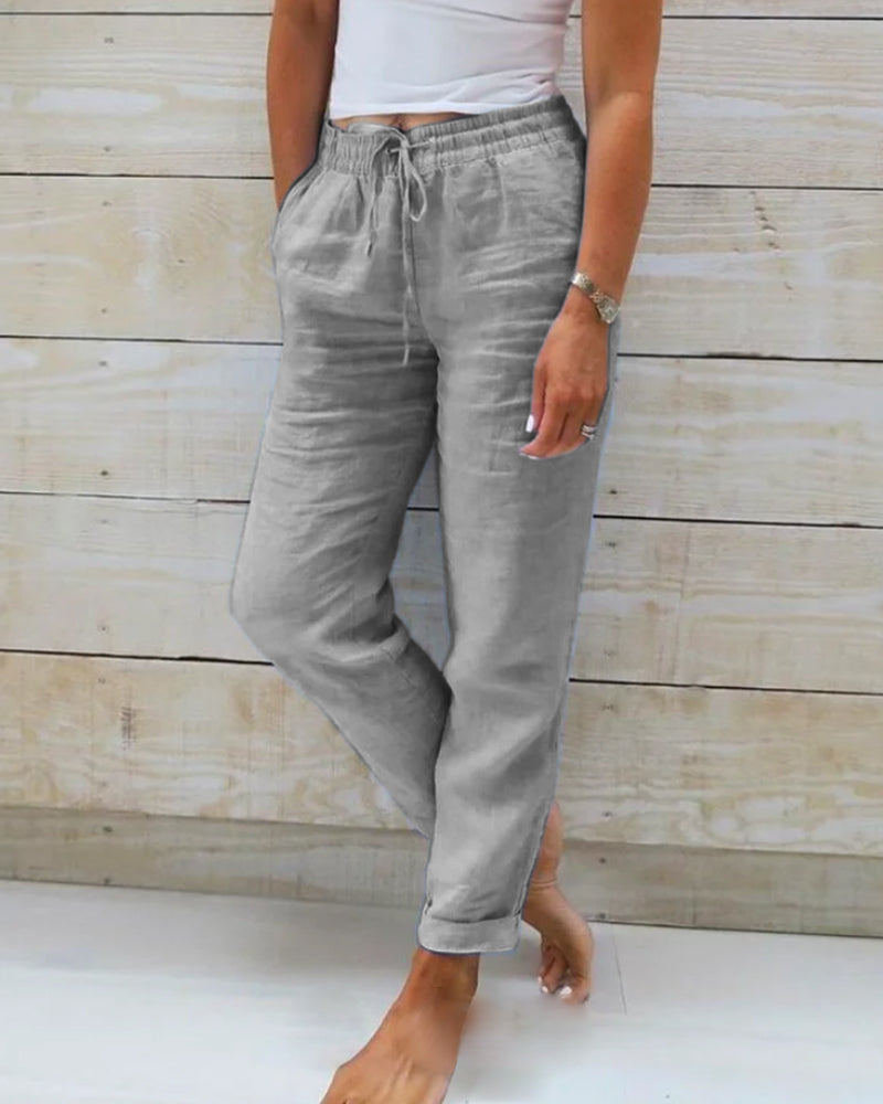 Un pantalon léger et élégant pour femme, de couleur grise, avec un cordon de serrage à la taille et une coupe décontractée, parfait pour un look moderne et confortable.
