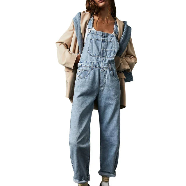Femme portant la combinaison moderne Veloria en jean bleu clair, style salopette ample avec bretelles et grandes poches, look casual superposé avec veste.