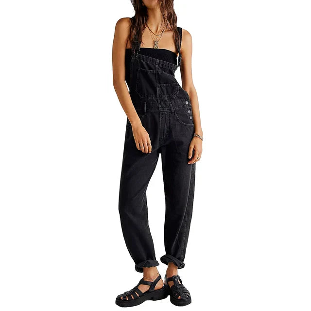 Femme portant la combinaison moderne Veloria en jean noir, style salopette ample à bretelles avec poches et boutons sur le côté, look casual avec sandales.