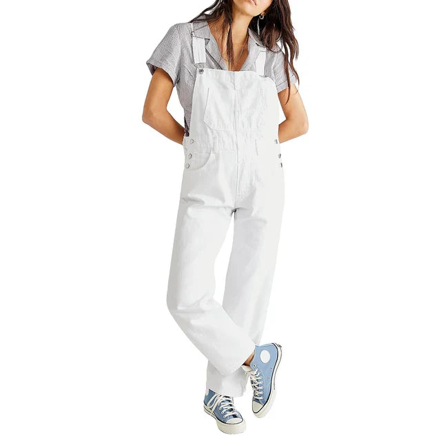 Femme portant la combinaison moderne Veloria blanche, style salopette ample à bretelles avec boutons sur les côtés, look casual avec t-shirt et baskets.