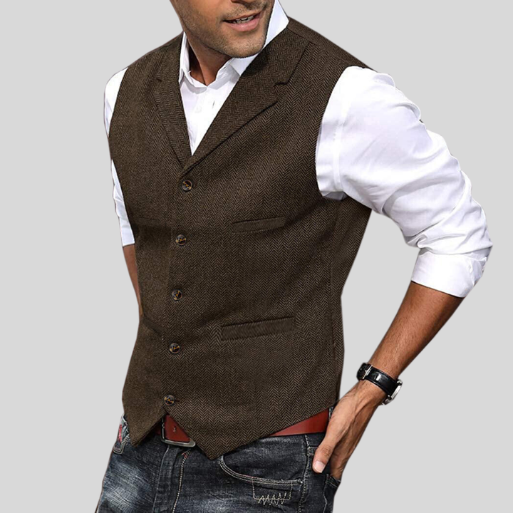 Gilet court pour hommes Virgile moderne, marron foncé à motif chevrons, coupe ajustée avec boutons et poches passepoilées, porté sur chemise blanche avec jean.