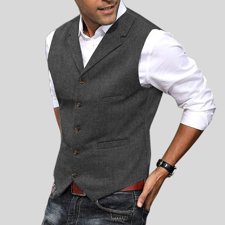 Gilet court pour hommes Virgile moderne, gris anthracite à motif chevrons, coupe ajustée avec boutons et poches, porté sur chemise blanche avec jean.