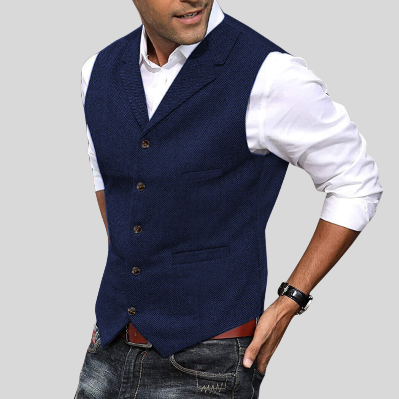 Gilet court pour hommes Virgile moderne, bleu marine à motif chevrons, coupe ajustée avec boutons et poches passepoilées, porté sur chemise blanche avec jean.