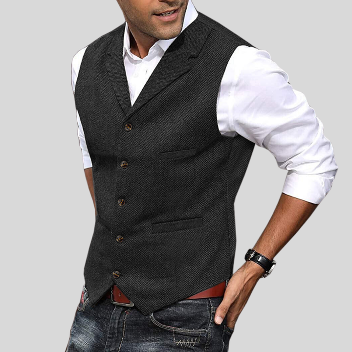 Gilet court pour hommes Virgile moderne, noir/gris foncé à motif chevrons, coupe ajustée avec boutons et poches, porté sur chemise blanche avec jean.