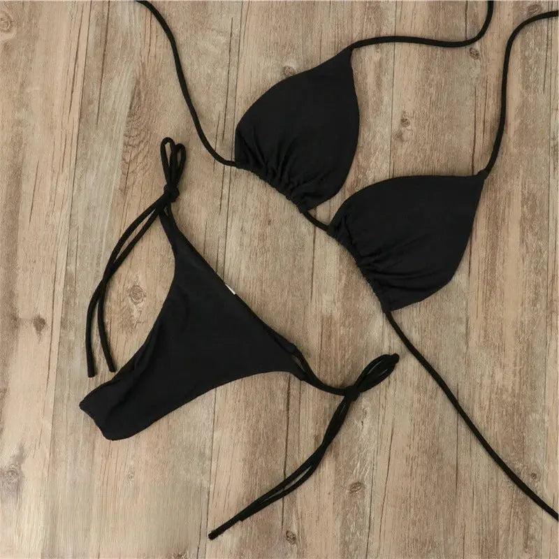 Ensemble bikini femme Virginie moderne de couleur noire, composé d’un haut triangle à liens ajustables et d’un bas à nouer sur les côtés, présenté à plat sur fond en bois pour un style sobre et élégant.