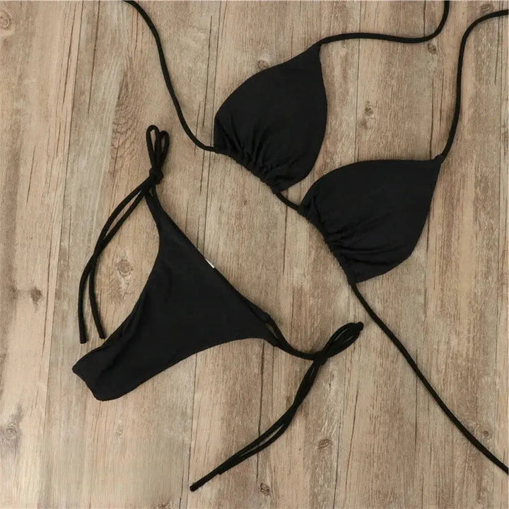 Ensemble bikini femme Virginie moderne de couleur noire, composé d’un haut triangle à liens ajustables et d’un bas à nouer sur les côtés, présenté à plat sur fond en bois pour un style sobre et élégant.