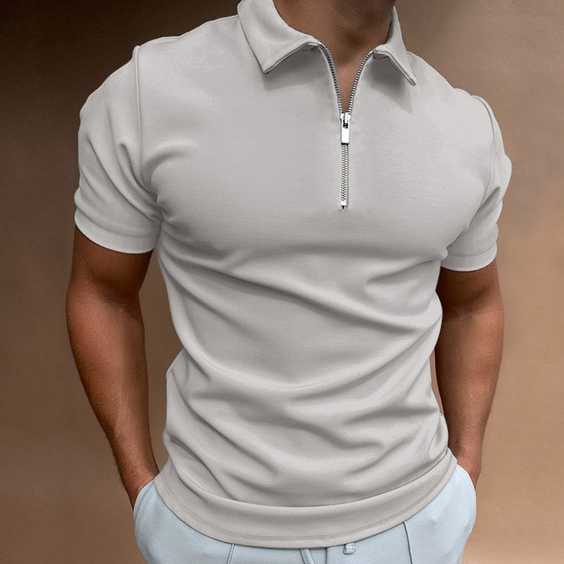 Polo pour homme beige clair à manches courtes, coupe ajustée et moderne, avec col structuré et fermeture zippée, porté avec un pantalon clair pour un look élégant, sobre et contemporain.